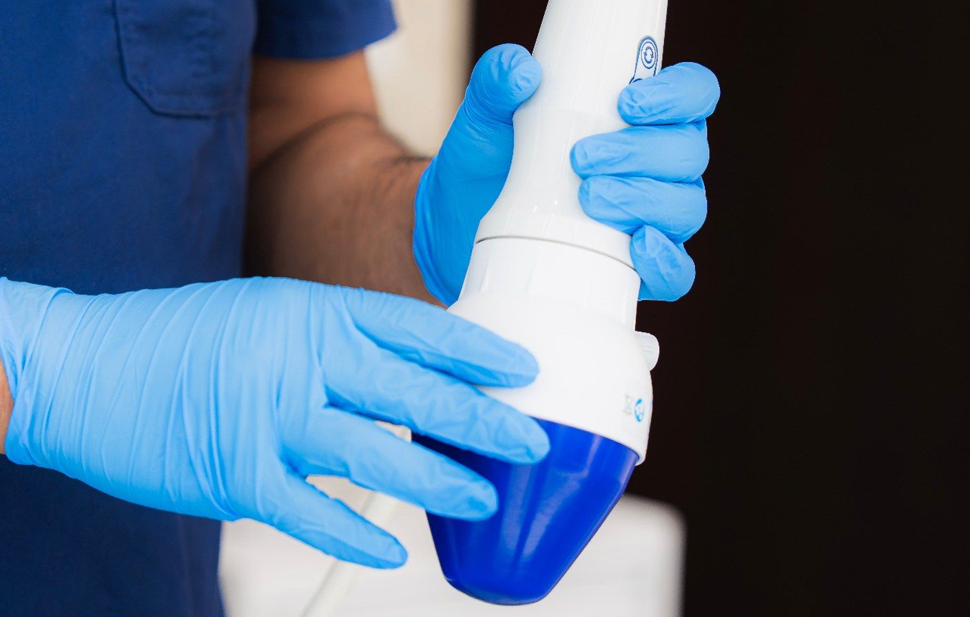 Clinician in blue scrubs and nitrile gloves holding a low-intensity shockwave therapy handpiece at Hisential.
