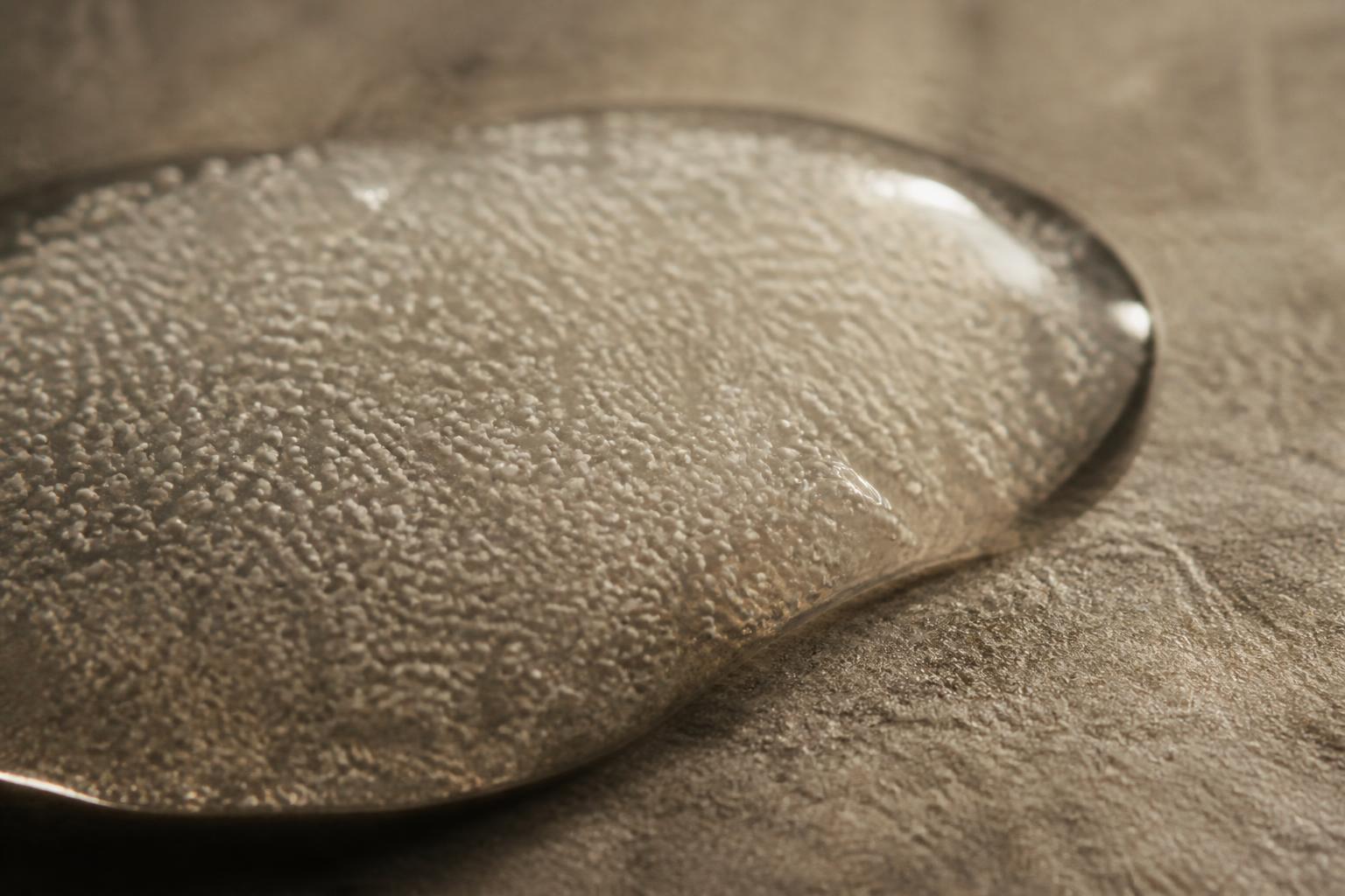 Abstract macro still life: pale microspheres suspended in a clear gel carrier, standing in for a calcium hydroxylapatite injectable.