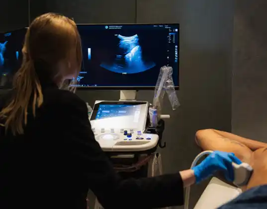 Clinician performing an ultrasound scan on a patient lying on an examination couch.